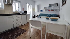Una cocina moderna con armarios blancos, microondas integrado y cafetera. Hay un comedor con una mesa blanca y sillas azules.