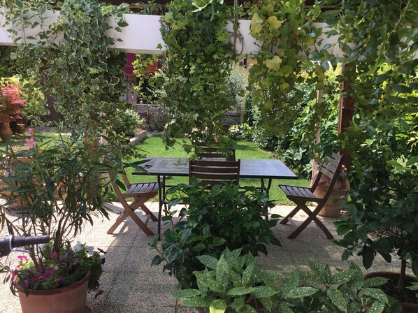 En terrasse med et bord og stole, omgivet af plantekasser og en græsplæne.