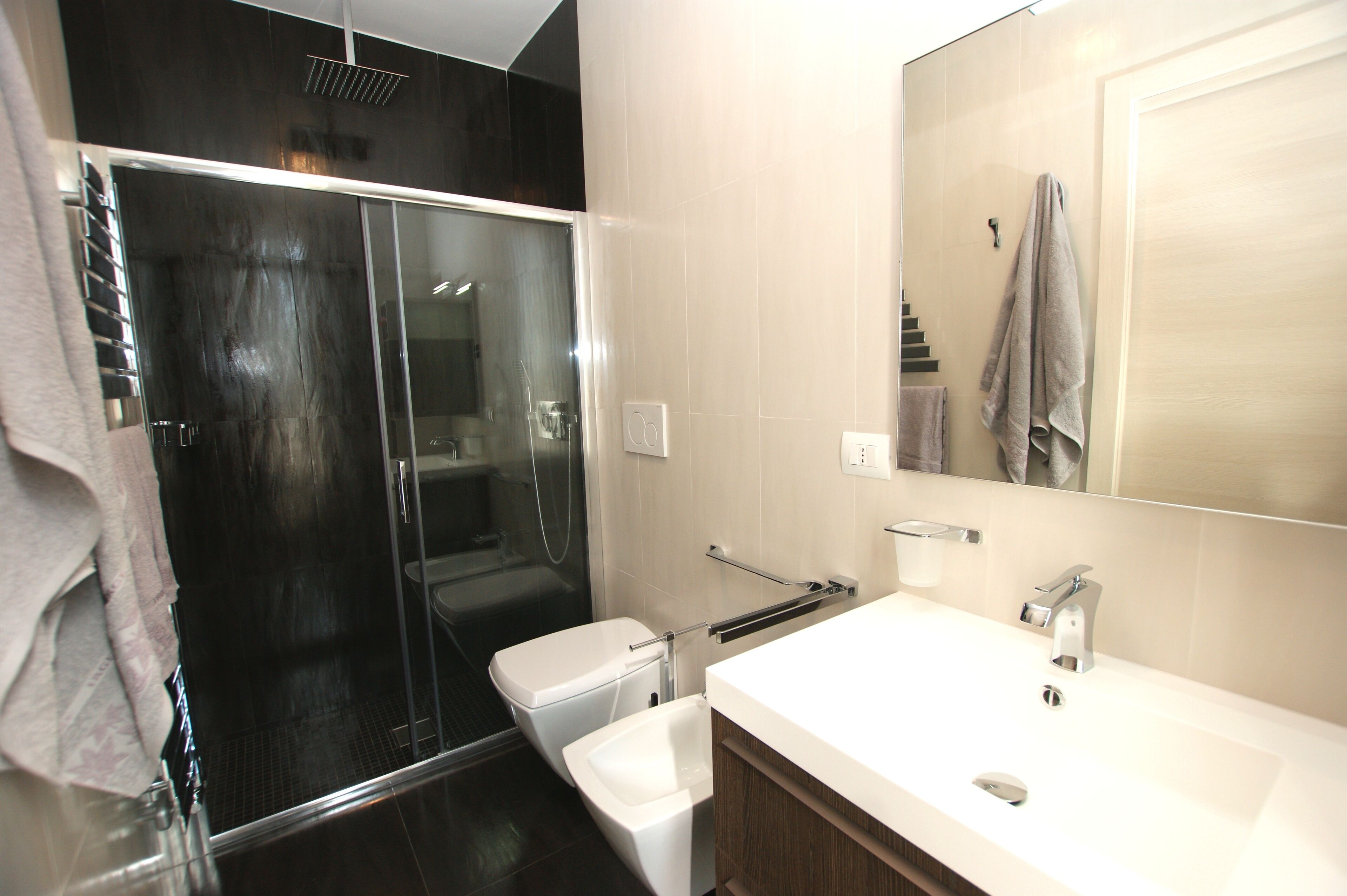 A modern bathroom with a glass-enclosed shower, a white sink, and a large mirror.