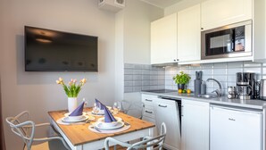 Et moderne køkken med hvide skabe, en mikrobølgeovn og en opvaskemaskine. Der er et spisebord med stole og en vase med blomster.