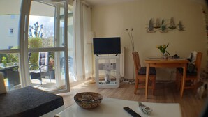 Un salon moderne doté d’une grande fenêtre, d’un téléviseur à écran plat, d’une table à manger avec des chaises et d’un saladier posé sur la table.