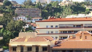 Ein mehrstöckiges Gebäude mit Balkonen, Bergen im Hintergrund und blauem Himmel.