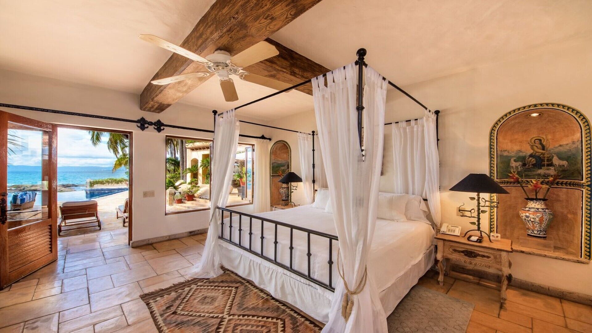 Un dormitorio con cama con dosel, ventilador de techo y vista al océano.