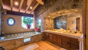 A bathroom with a stone wall, a bathtub, a large mirror, and wooden cabinets. - Gated Beachfront luxury Villa fully staffed for the vacation of your dreams (Puerto Vallarta)