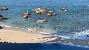 A clear view of a beach with a pool in the foreground, surrounded by rocky outcrops and calm sea. - Gated Beachfront luxury Villa fully staffed for the vacation of your dreams (Puerto Vallarta)