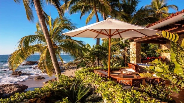 A beachside patio with a table and chairs, surrounded by palm trees and ocean views. - Gated Beachfront luxury Villa fully staffed for the vacation of your dreams (Puerto Vallarta)
