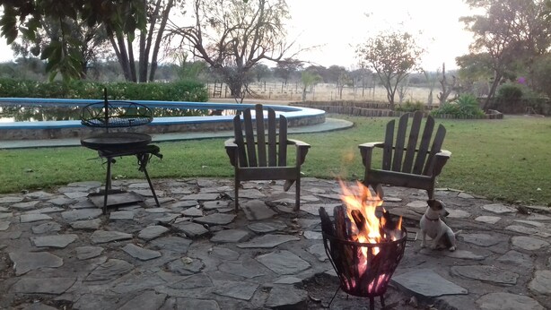 A stone patio with a fire pit, two Adirondack chairs, and a grill.