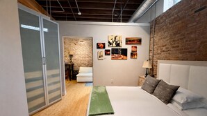 A modern bedroom with a large bed, a brick wall, and artwork on the wall. - Downtown Music City Loft living! ~Steps to the Ryman and Broadway (Nashville)