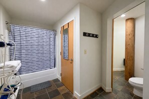 A bathroom with a bathtub, a shower curtain, a towel rack, and a wooden accent wall. - Downtown Music City Loft living! ~Steps to the Ryman and Broadway (Nashville)