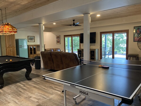 A spacious room with a pool table, a ping pong table, a brown leather couch, and a ceiling fan.