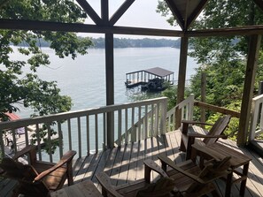 A wooden deck with chairs and a gazebo overlooking a lake with a dock and boat.