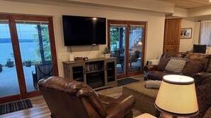 A living room with a leather sofa, a wooden coffee table, a television, and a view of the outdoors. - Lakefront Retreat w/ Private Dock, Game Room & Sunset Views - Sleeps 16 (Winchester)