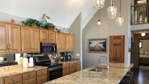 A kitchen with wooden cabinets, a granite countertop, a built-in oven, a microwave, a coffee maker, and a hanging light fixture. - Lakefront Retreat w/ Private Dock, Game Room & Sunset Views - Sleeps 16 (Winchester)