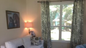Una sala de estar con un sofá blanco, una mesa de centro redonda y una ventana con cortinas estampadas.