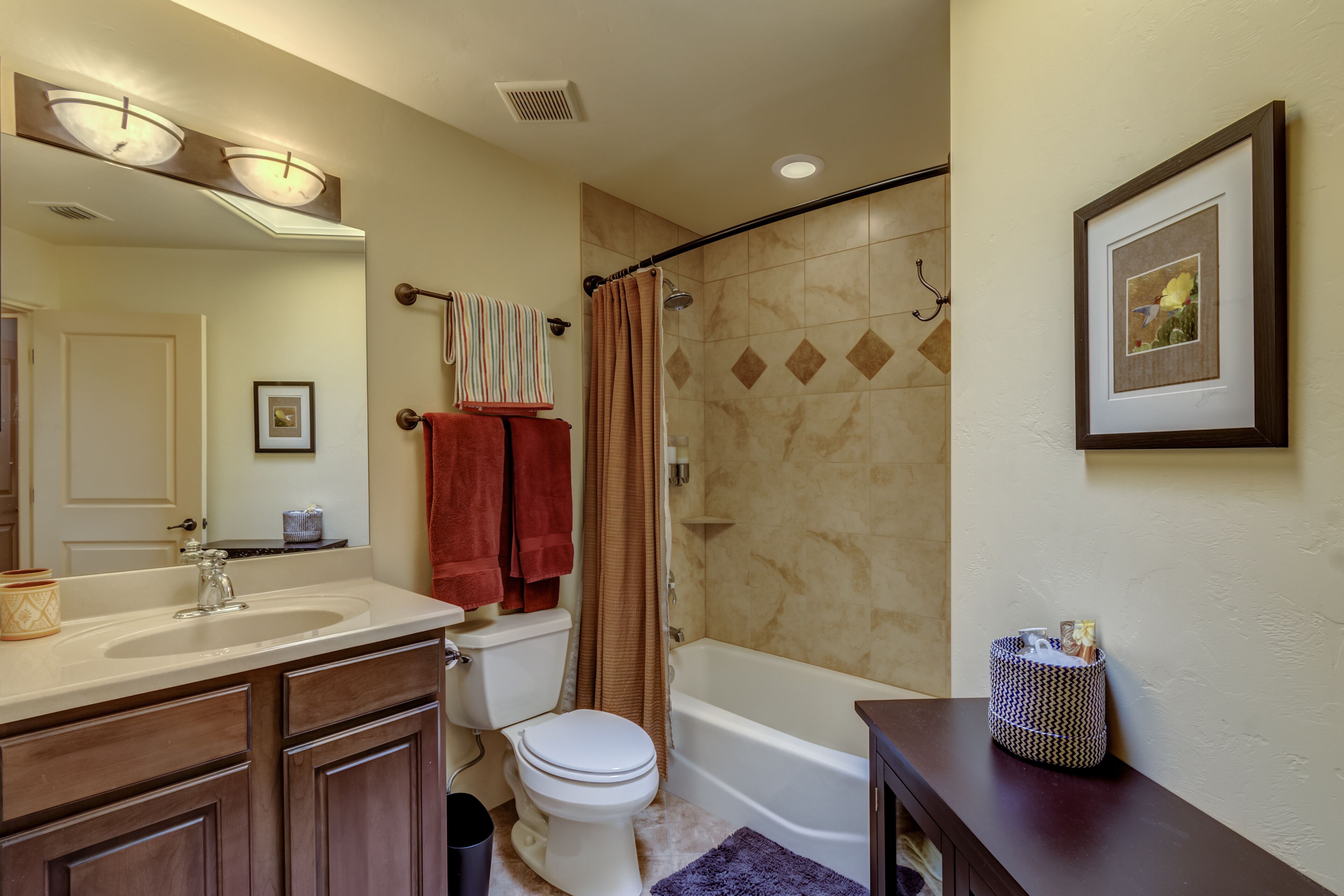 Une salle de bain équipée d’un lavabo, de toilettes, d’une baignoire et d’une douche. On y trouve un porte-serviettes avec des serviettes, un tableau encadré au mur et un petit panier posé sur le meuble-lavabo.