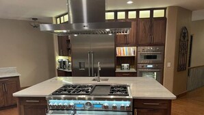 Une cuisine moderne dotée d’un îlot central, d’appareils électroménagers en acier inoxydable et de meubles de rangement en bois.