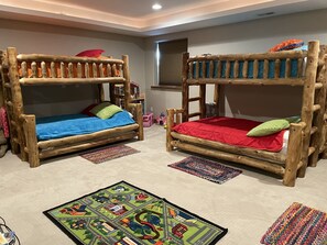 A room with two bunk beds made of wood, each with a mattress and pillows. There are colorful rugs on the floor and a map rug in front of the beds. - Large, luxury cabin, sleeps 19 with a gourmet kitchen, hot tub & fire pit (Angel Fire)