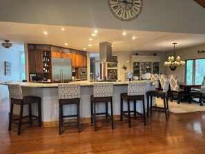 A modern kitchen with a central island, bar stools, and a dining area with a chandelier. - Large, luxury cabin, sleeps 19 with a gourmet kitchen, hot tub & fire pit (Angel Fire)