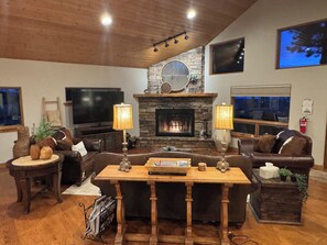 A cozy living room with a stone fireplace, leather sofas, a wooden coffee table, and a television. - Large, luxury cabin, sleeps 19 with a gourmet kitchen, hot tub & fire pit (Angel Fire)