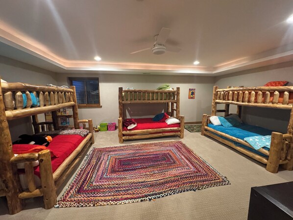 Une pièce avec trois lits superposés, un ventilateur de plafond et un tapis coloré en fibres tressées.