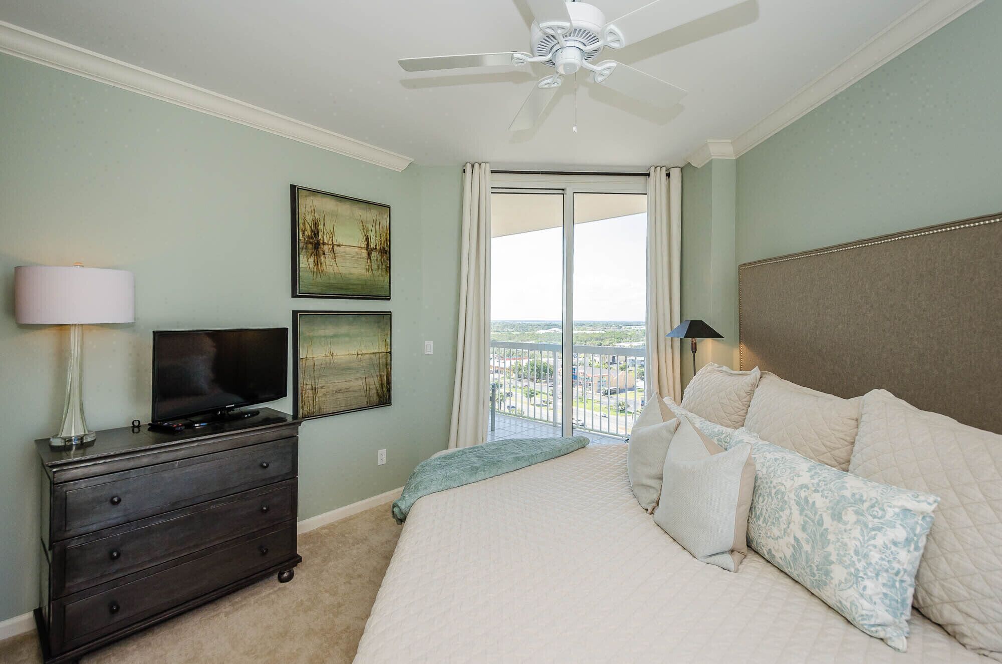 A bedroom with a bed, a dresser, a television, and a ceiling fan.