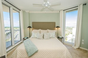 A bedroom with a large bed, a ceiling fan, and a view of a cityscape through large windows. - FIRST WEEK OF AUGUST JUST OPENED! (Destin)