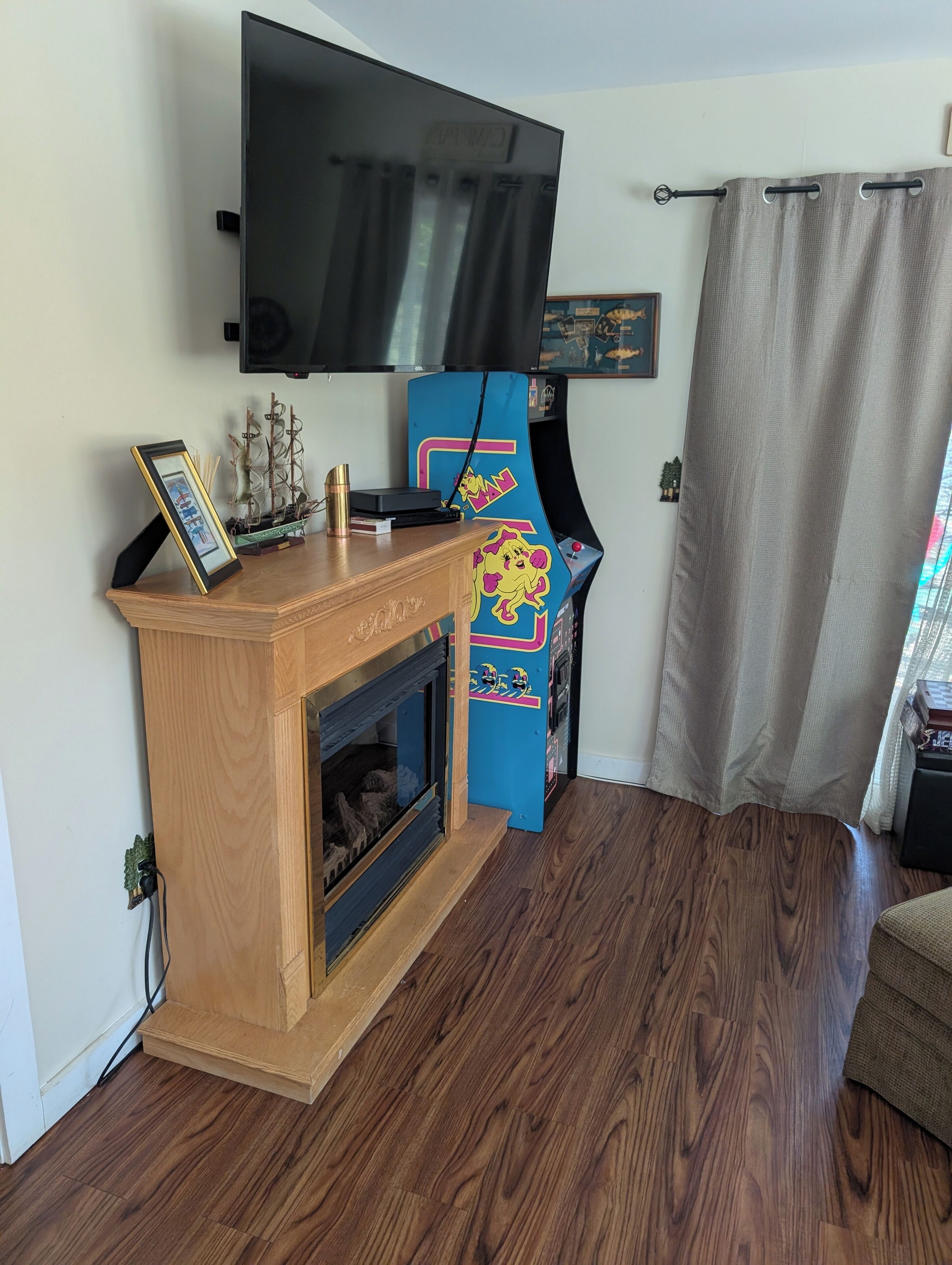 Un salon comprenant un meuble de rangement en bois pour les appareils multimédias, un téléviseur à écran plat fixé au mur, une petite cheminée et une console de jeux.
