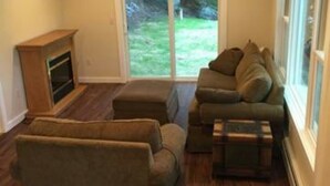A living room with a fireplace, a sofa set, and a view of a grassy yard through a sliding glass door.
