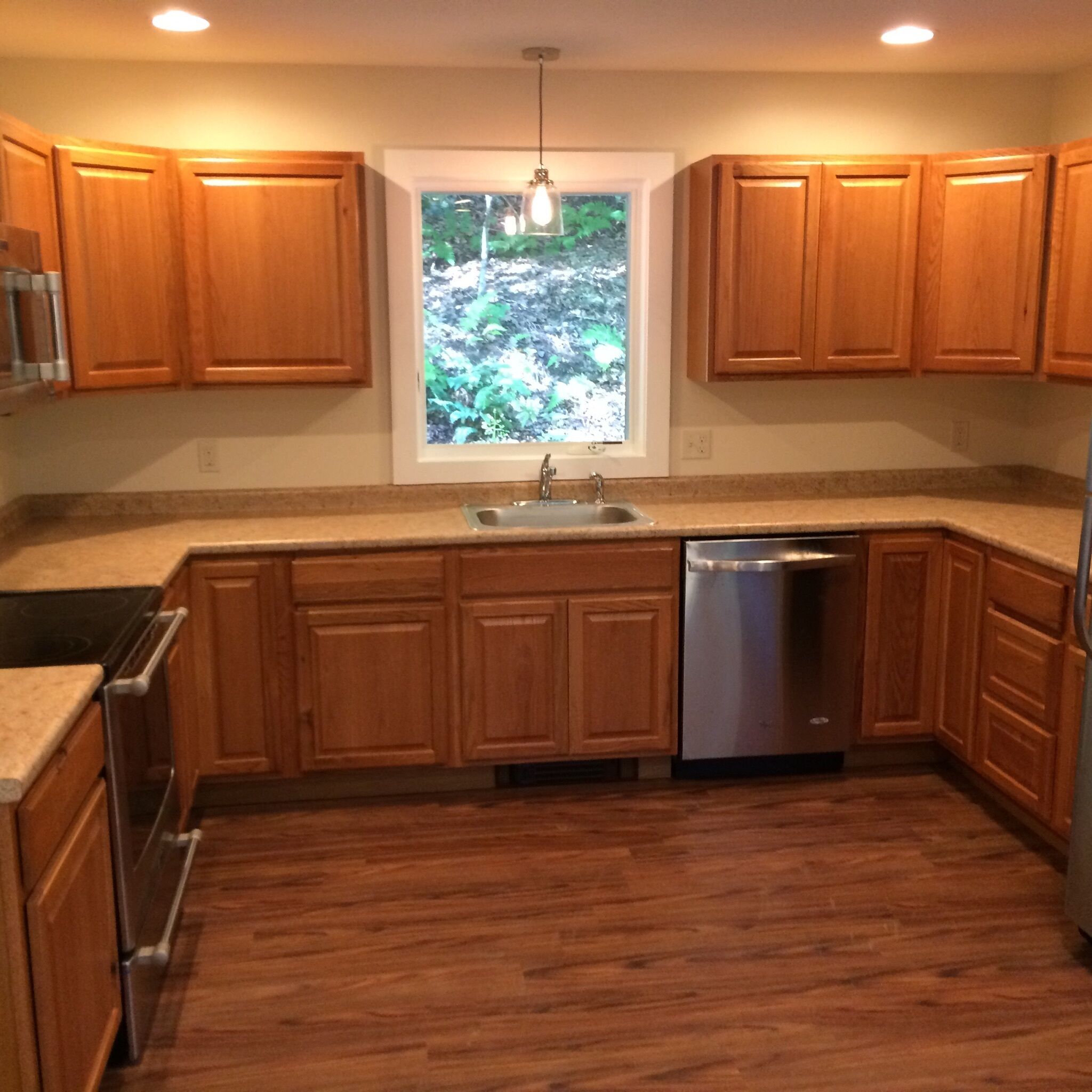 A kitchen with wooden cabinets, a stainless steel dishwasher, and a window with a view of greenery.