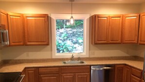 A kitchen with wooden cabinets, a stainless steel dishwasher, and a window with a view of greenery.