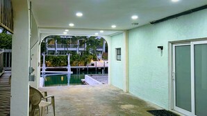 Un espacio al aire libre techado con piscina, una silla y una puerta que da a un porche cubierto.