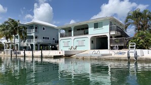 Una propiedad frente al agua con piscina, un barco y un edificio de varios pisos con balcones.