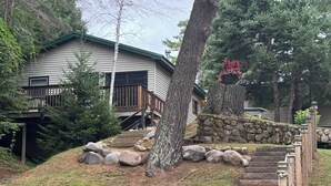 Una casa de dos pisos con un muro de contención de piedra y escaleras de madera que llevan a una terraza.
