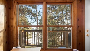 Habitación de cabaña de madera con un ventanal grande que da a una terraza y bosque.