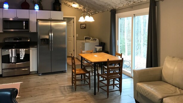 Une cuisine moderne dotée d’appareils électroménagers en acier inoxydable, un coin repas avec des chaises en bois et une grande fenêtre offrant une vue sur l’extérieur.