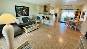 A living room with a sofa, coffee table, and a painting on the wall. There is a kitchen area with a dining table and chairs. - Private Heated  Pool House 6 miles from the Beach (Bradenton)