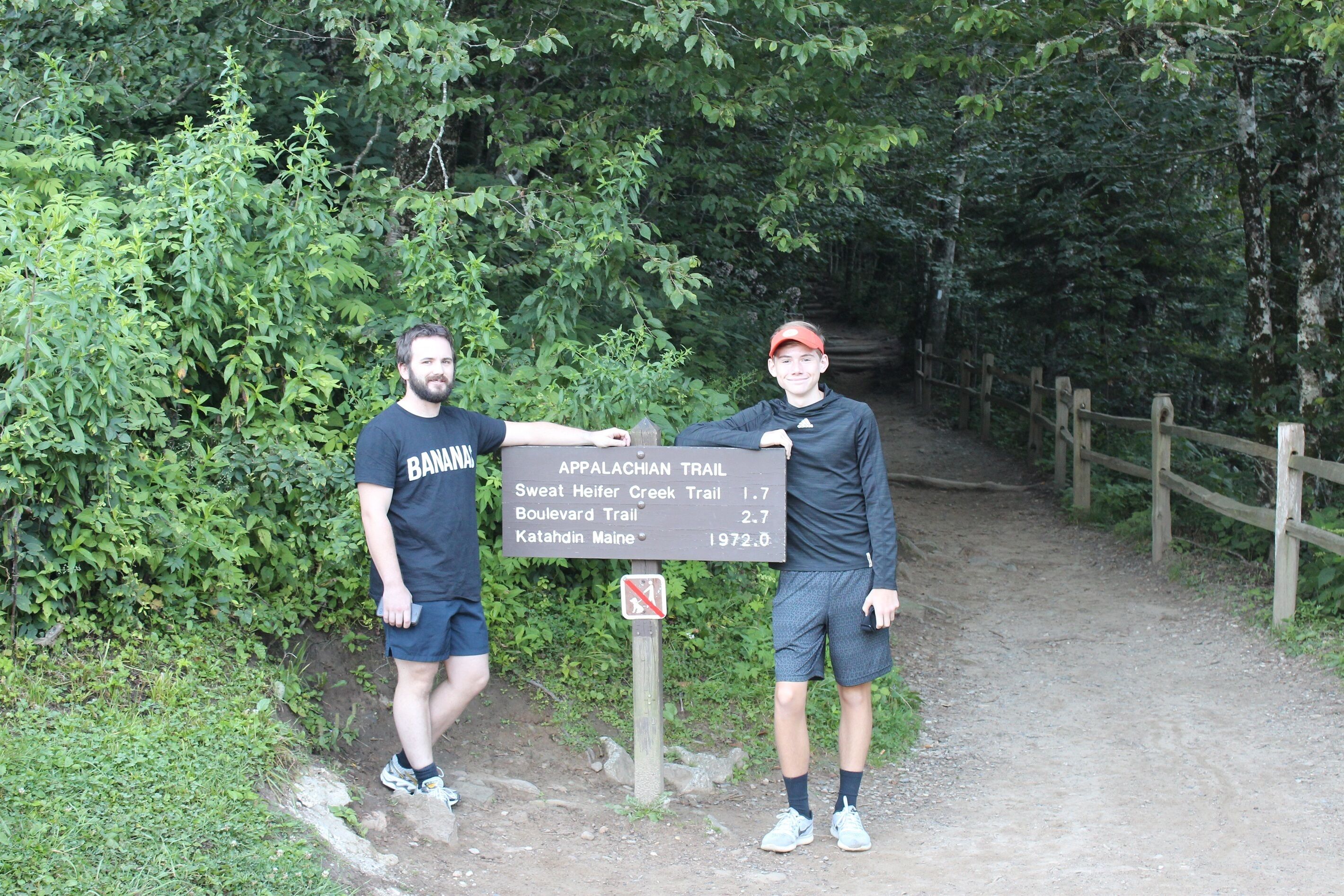 Two people standing next to a trail sign with information on different trails.