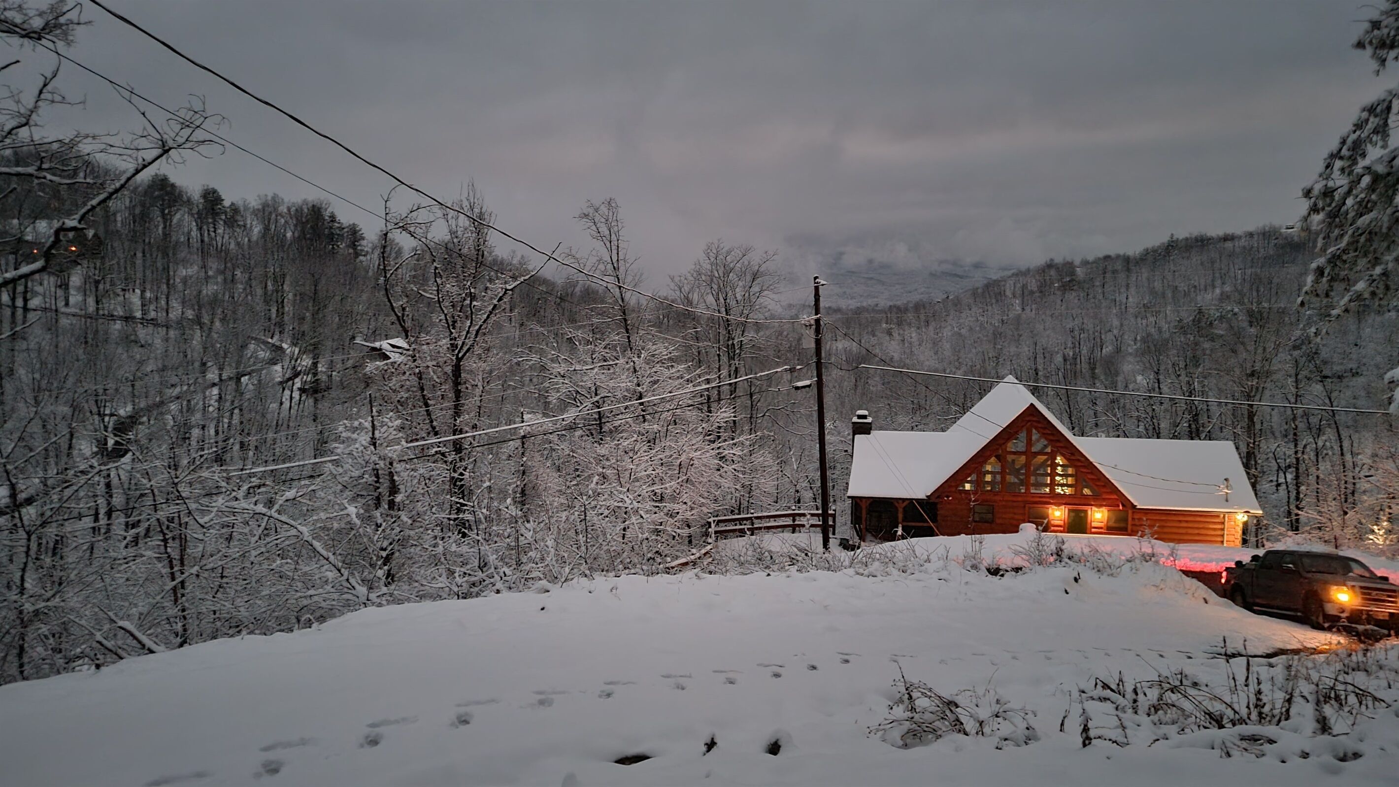 Une cabane en rondins dont le toit est recouvert de neige, entourée d’une zone boisée.