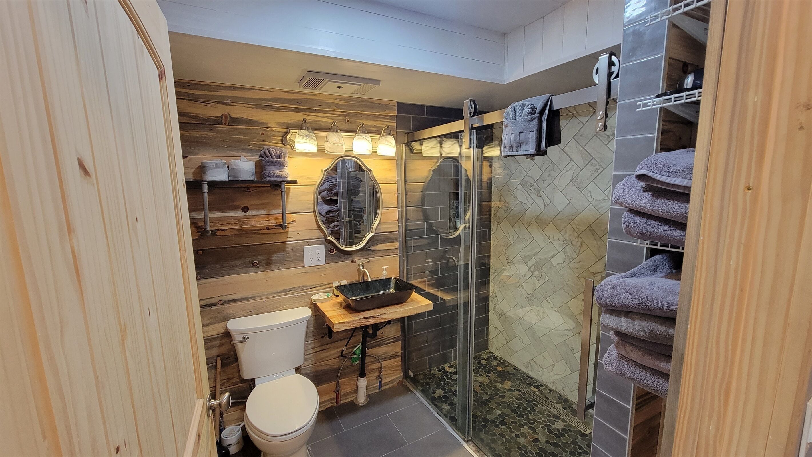 Une salle de bain avec un meuble-lavabo en bois, une cabine de douche en verre et un carrelage au sol.