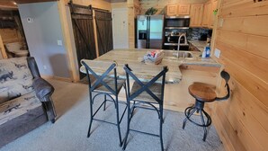 L’intérieur de ce chalet rustique est agrémenté de boiseries, et comprend un coin cuisine équipé d’appareils modernes, ainsi qu’un espace détente avec une table et des chaises.