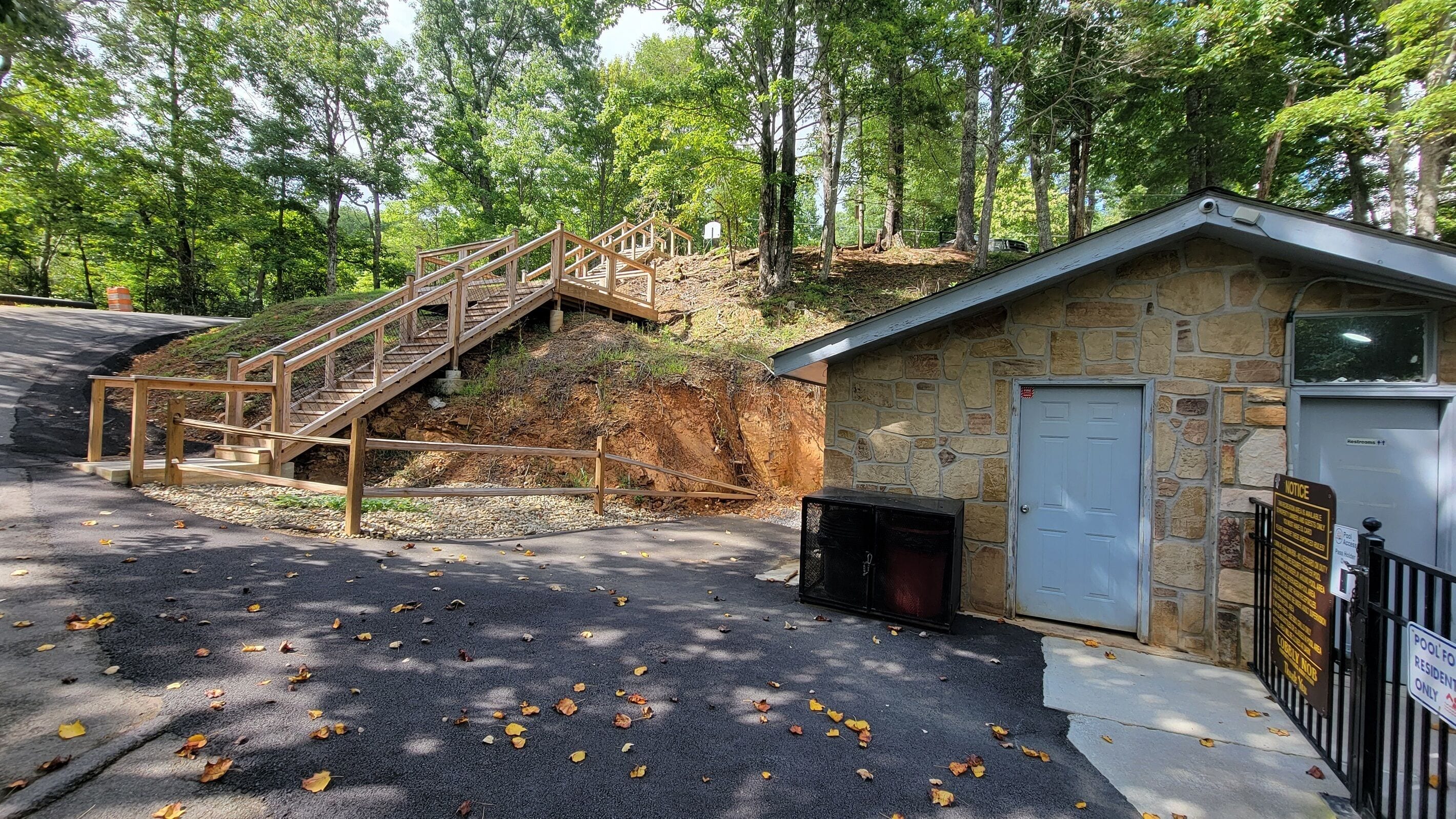 Un bâtiment en pierre avec un escalier en bois menant à un niveau supérieur, un petit espace couvert et un panneau indiquant qu’une piscine est réservée aux résidents.