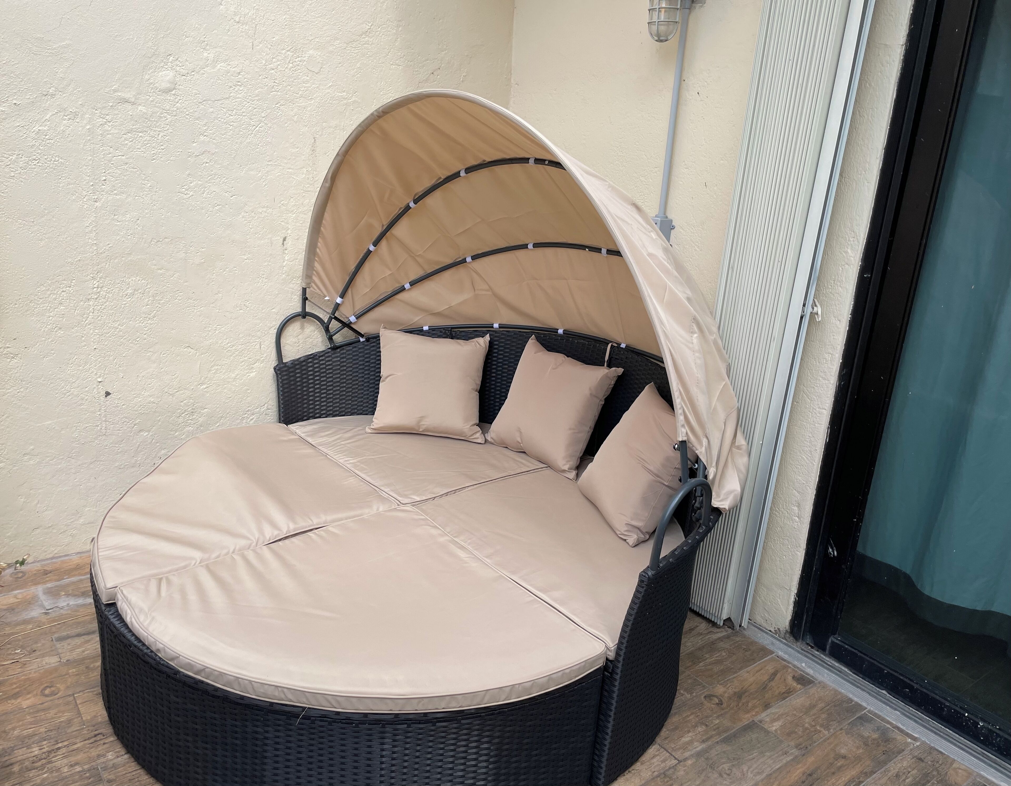 Een terras met ronde zithoek, voorzien van een zonnescherm, comfortabele kussens en een rieten frame.