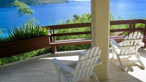 A wooden deck with two Adirondack chairs facing a large body of water and a distant island. - Paradise At A Great Price, Amazing Renovated Waterfront Escape: Private Balcony! (St. Thomas)