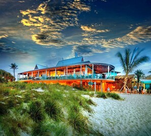 A beachfront building with a curved roof, multiple balconies, and a sandy beach in the foreground. - Perfect home away, modern amenities, Salt Heated Pool ~ Close to S. Venice Beach (South Venice)