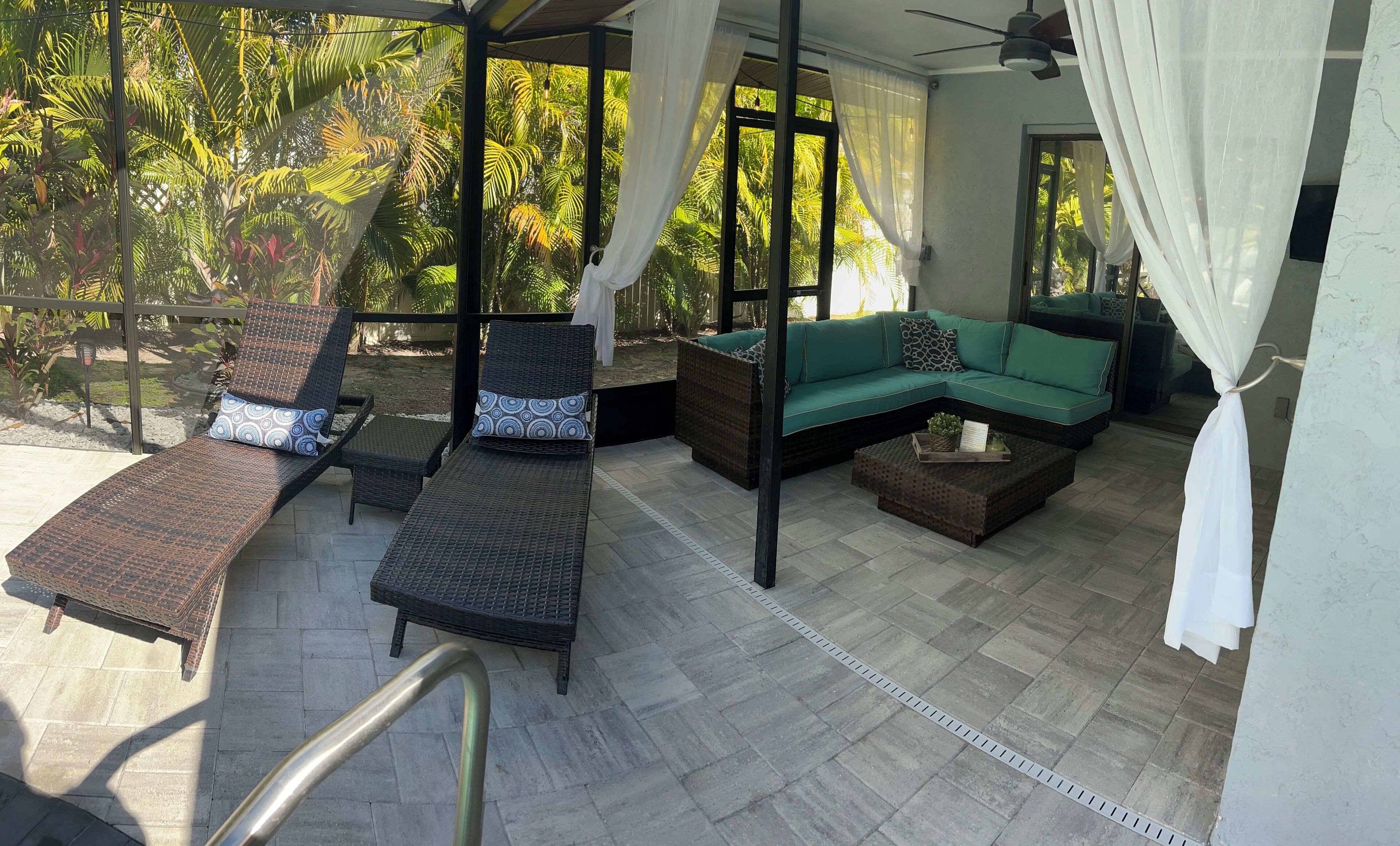 Uma área externa iluminada pelo sol, com mobiliário de vime, um sofá verde e um ventilador de teto.