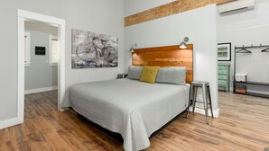 A bedroom with a wooden headboard, a bed with a grey quilt, a small stool, and a wall-mounted lamp. - Contemporary Chic │West Side │Walk Everywhere │Hot Tub │One Block to River (Bend)