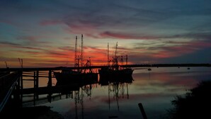 Un puerto deportivo al atardecer con barcos amarrados, agua tranquila que refleja el cielo y un muelle de madera.