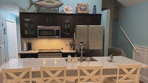 Una cocina moderna con armarios oscuros, electrodomésticos de acero inoxidable y una isla central con cuatro sillas.