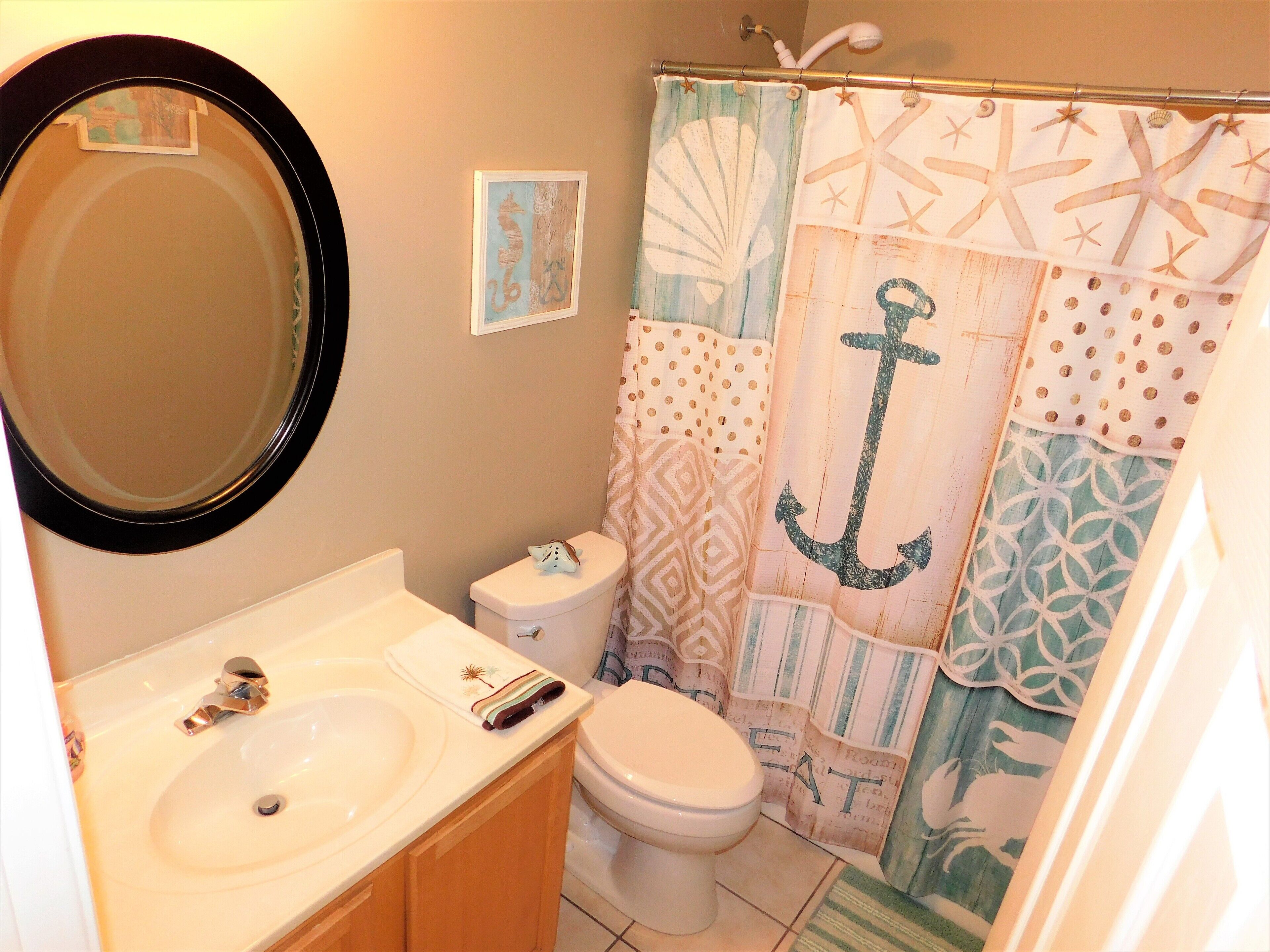 A bathroom with a round mirror, a sink, a toilet, and a shower curtain with nautical designs.