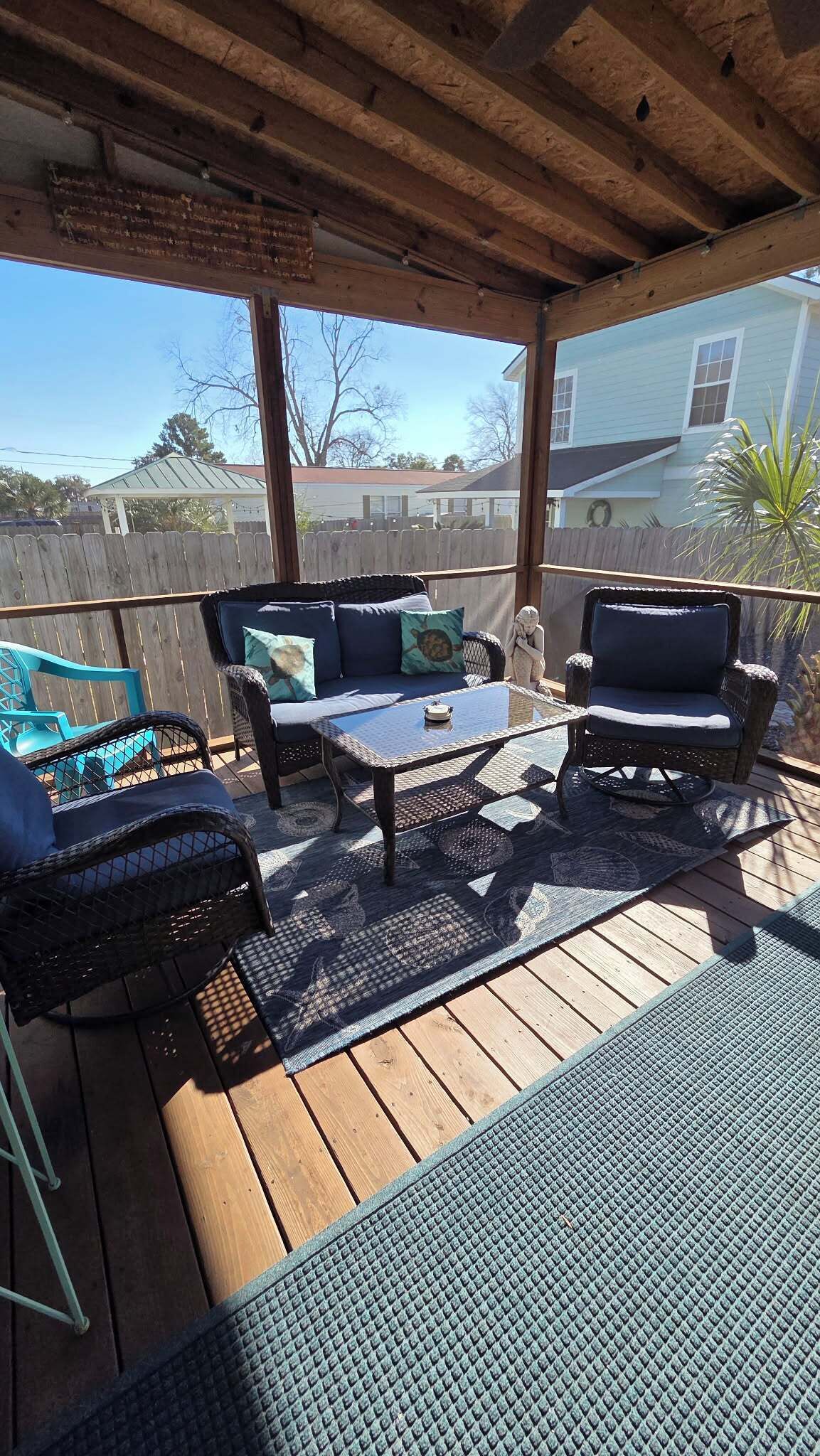 A covered patio with wicker furniture, a glass coffee table, and a view of a house.